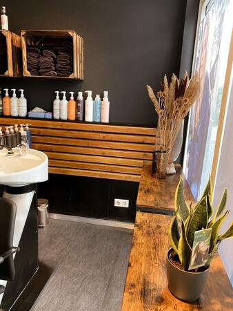 Moderner Friseursalon mit Holzregalen, Handtüchern, Pflegeprodukten und Zimmerpflanzen.